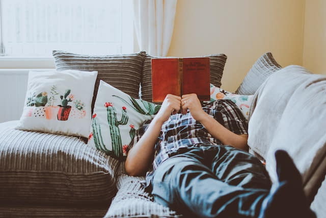 man reading book on couch, hiding face